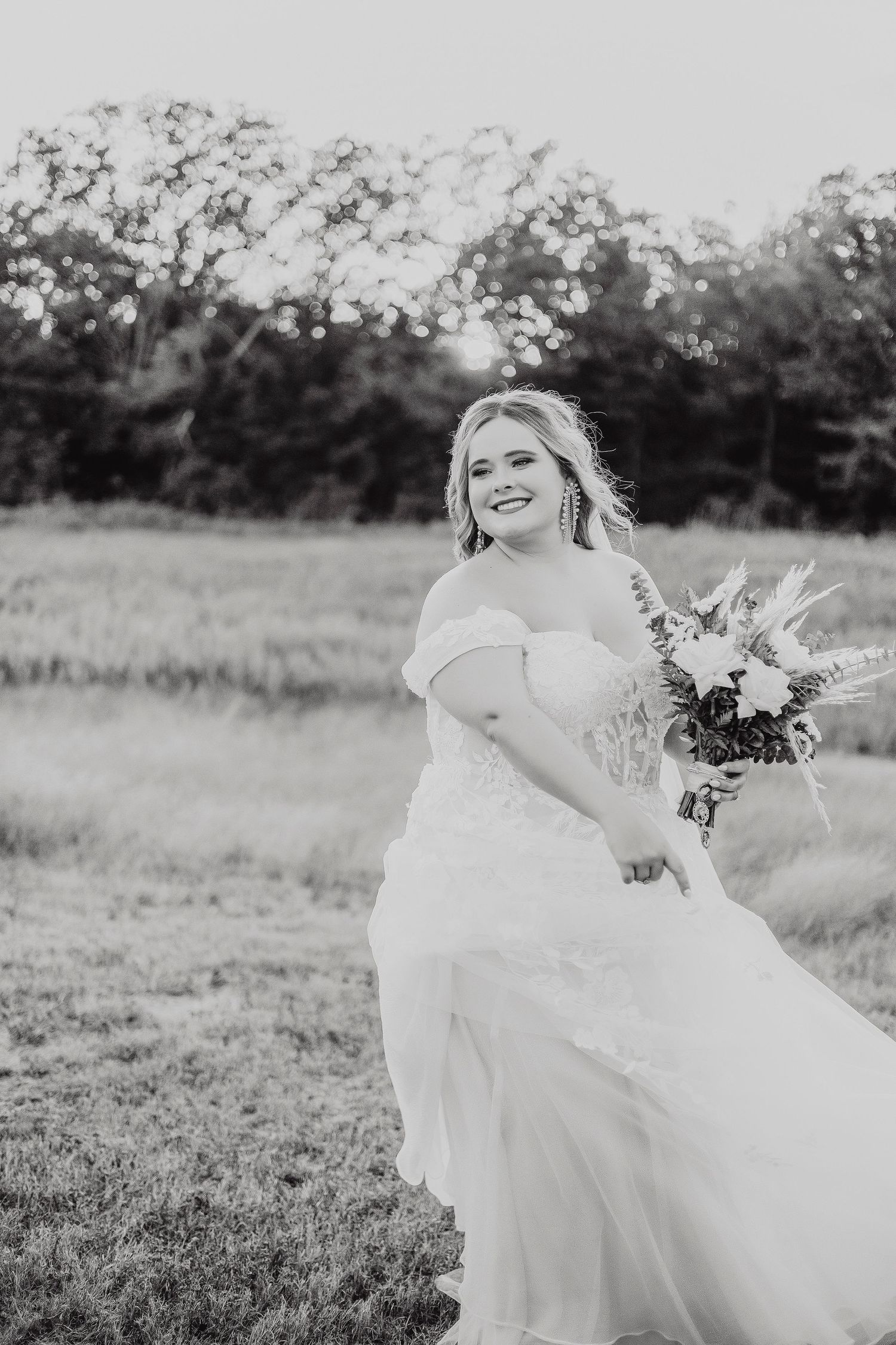 Bride in flowing white dress twirling in a sunlit meadow during golden hour.