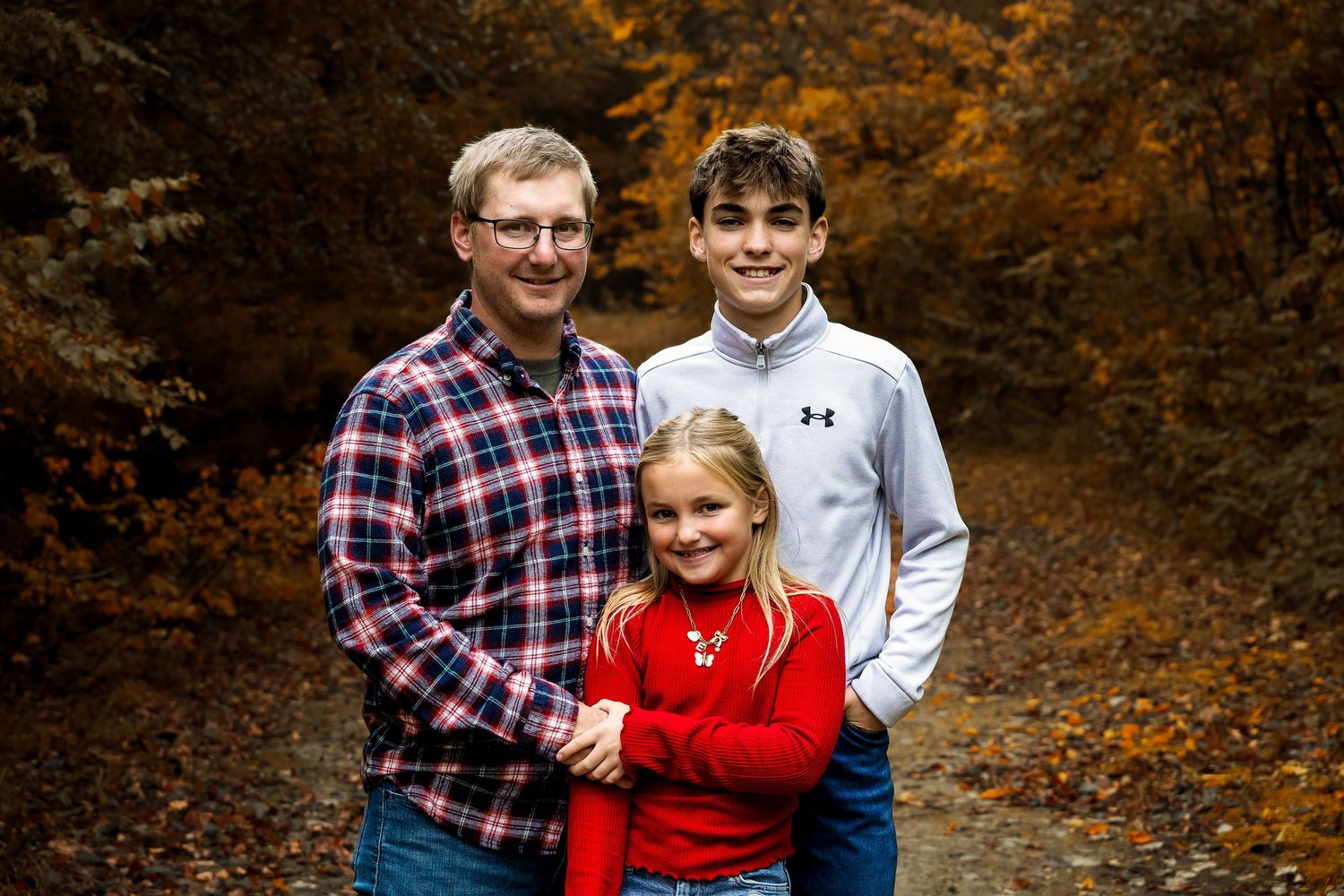 A family group poses together on a wooded autumn path with fallen orange and brown leaves.