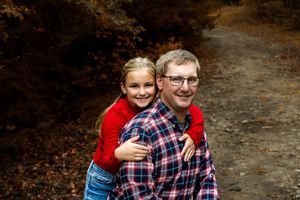 People in plaid and red clothing embrace and smile while posing outdoors in an autumn setting.