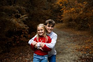 Two people share a playful moment on a wooded path surrounded by autumn foliage.