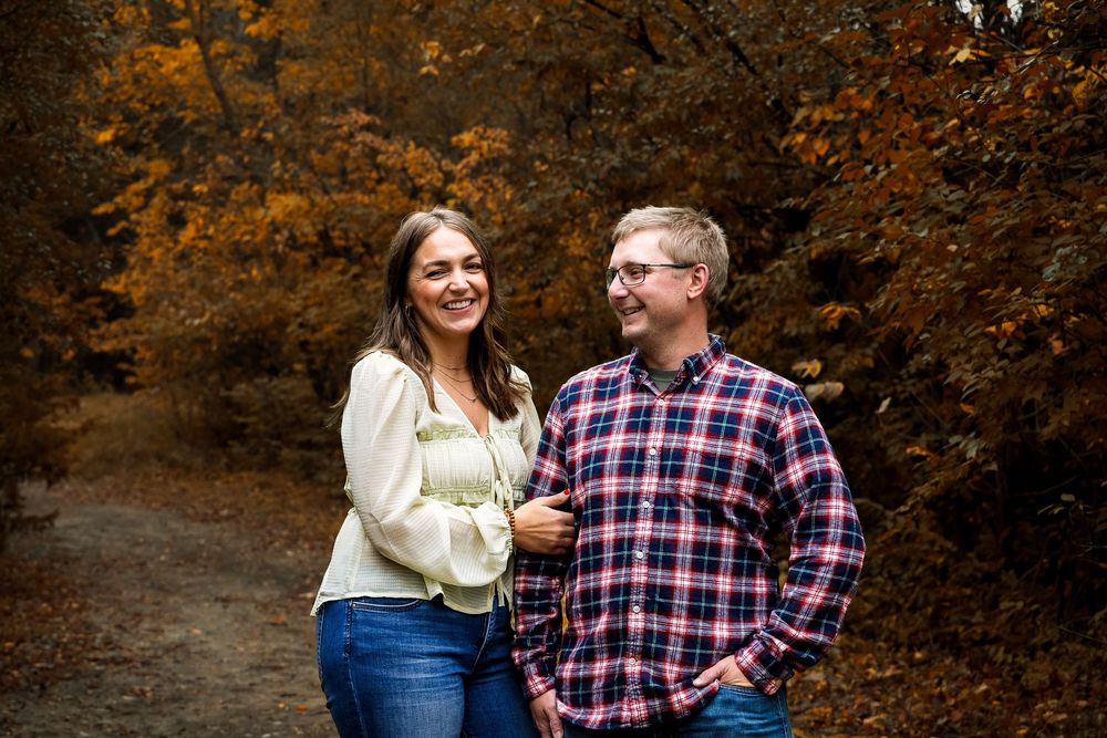 A couple shares a romantic moment together in a park surrounded by autumn foliage and golden light.