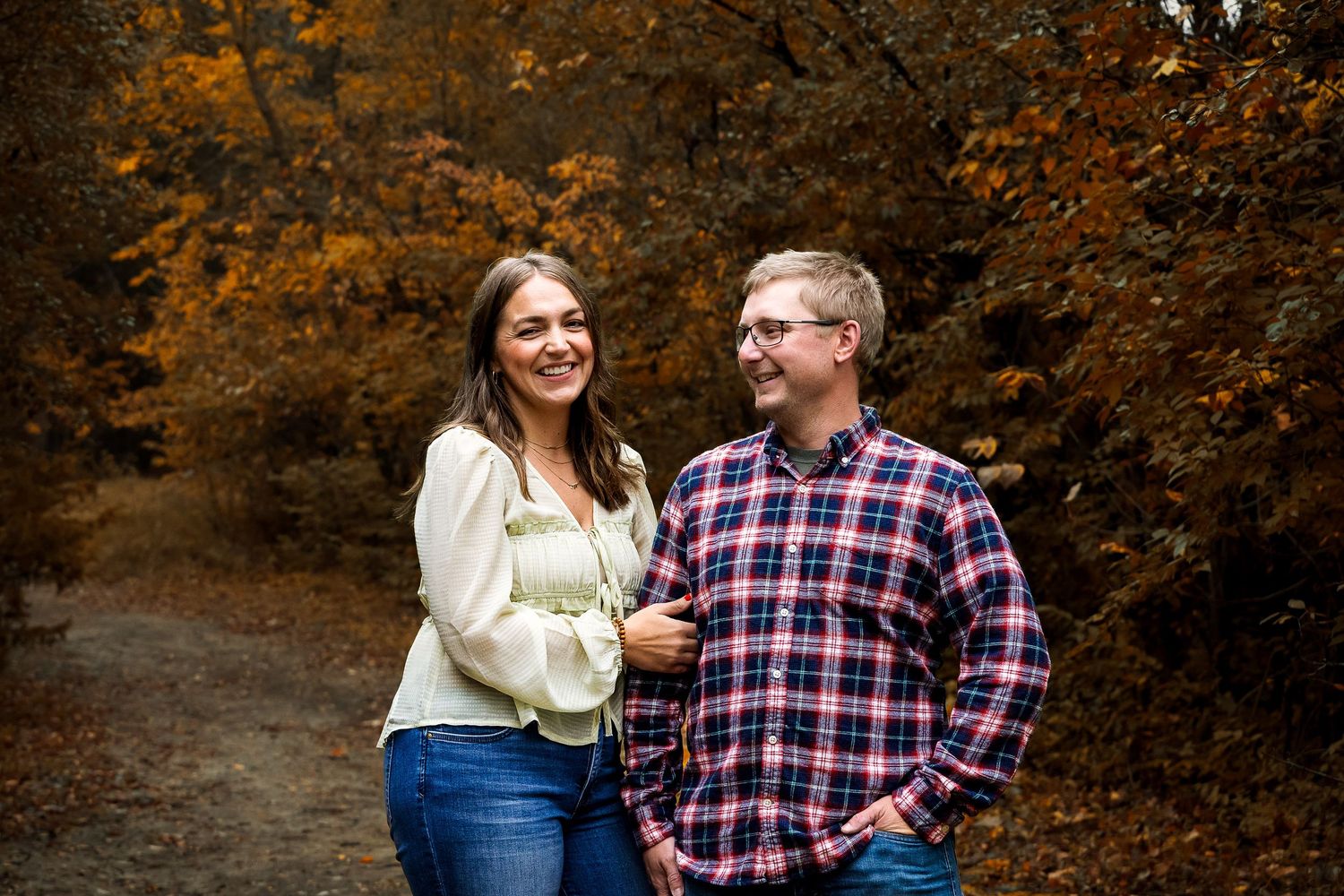 A couple shares a romantic moment together in a park surrounded by autumn foliage and golden light.