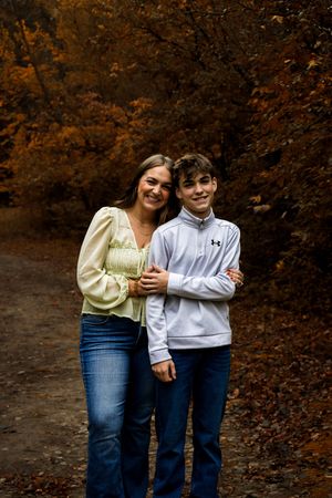 A pair in matching jeans share a candid moment together against an autumn forest backdrop.