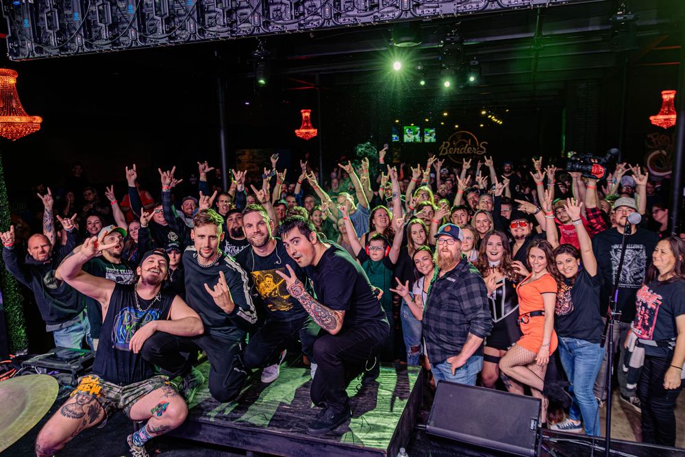 Enthusiastic crowd with raised hands at a packed indoor concert venue.
