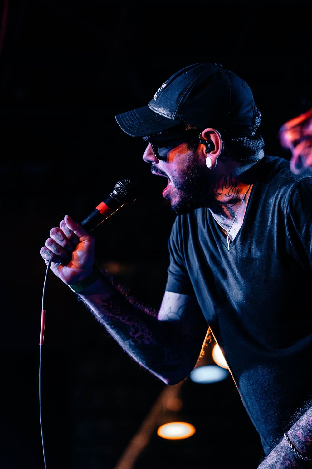 Singer in black cap and t-shirt performs passionately on dark stage with dramatic lighting.