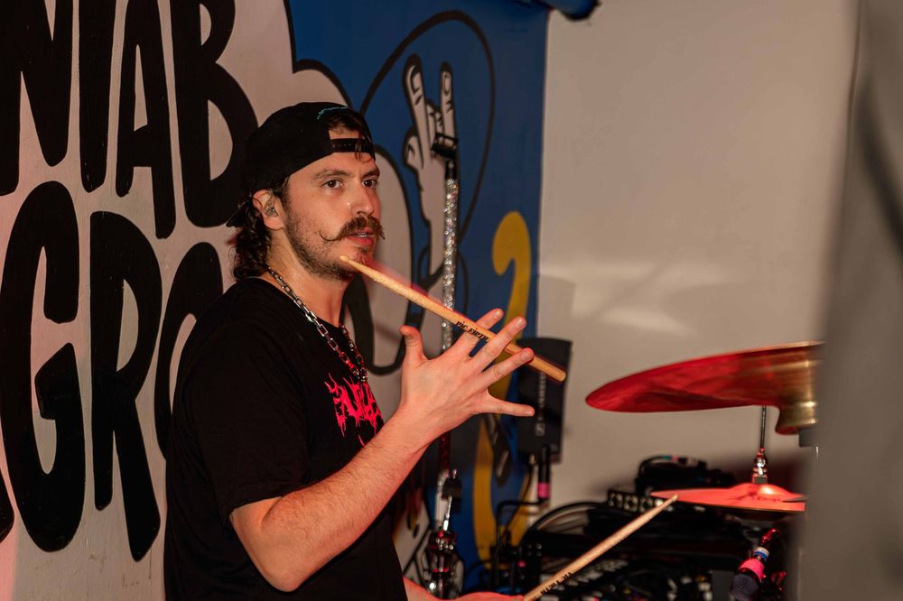 Musician in a black hat gestures while performing in front of a painted backdrop.