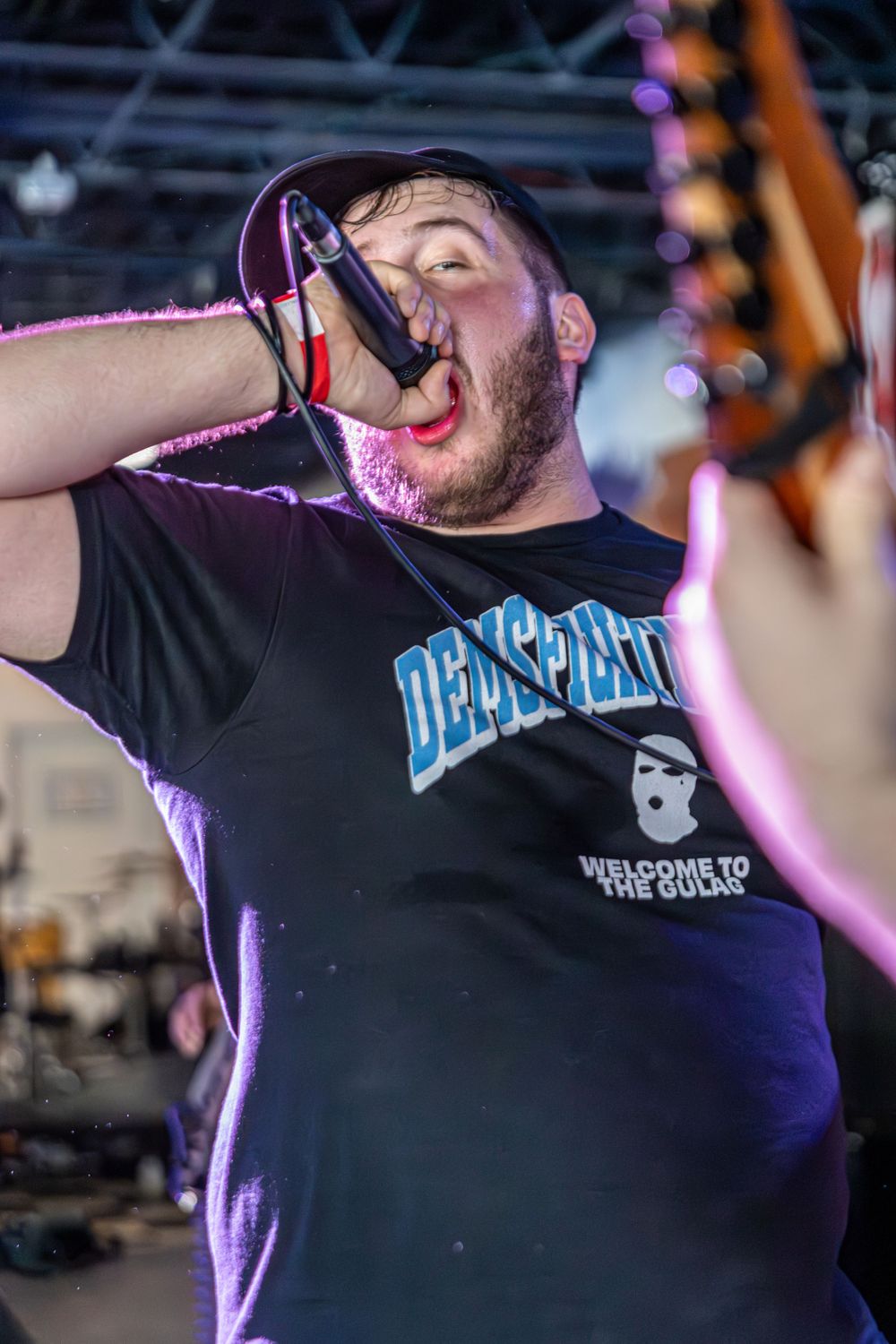 Vocalist in black band shirt performing energetically under stage lights.