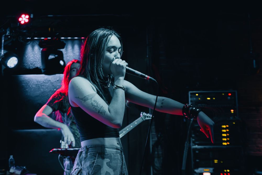 A performer singing passionately on stage with dramatic concert lighting.