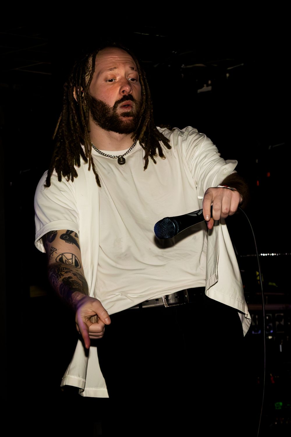 Musician in white shirt performing on stage in dramatic low lighting.