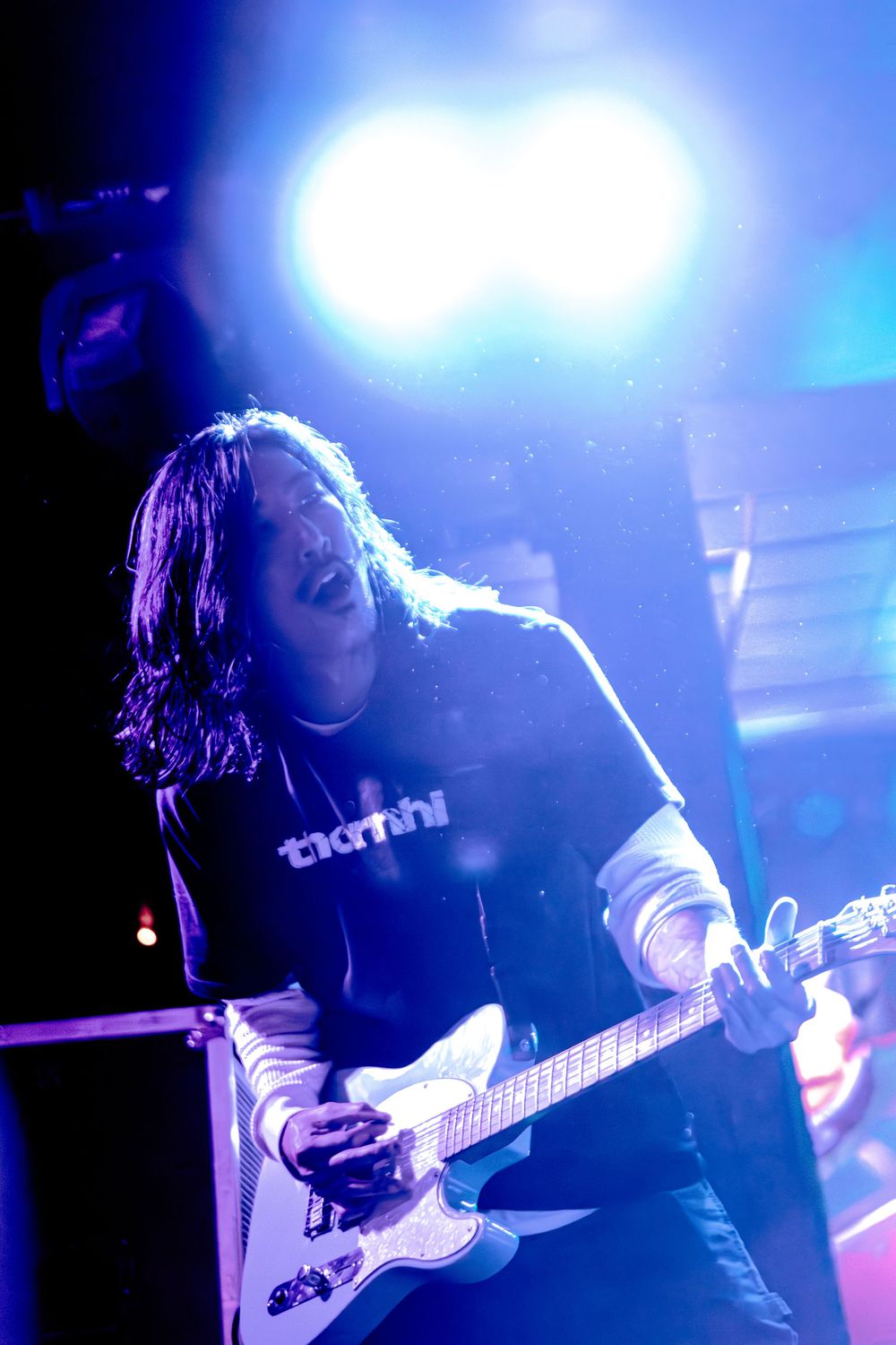 Guitarist performing on stage backlit by blue lights creating dramatic silhouette.