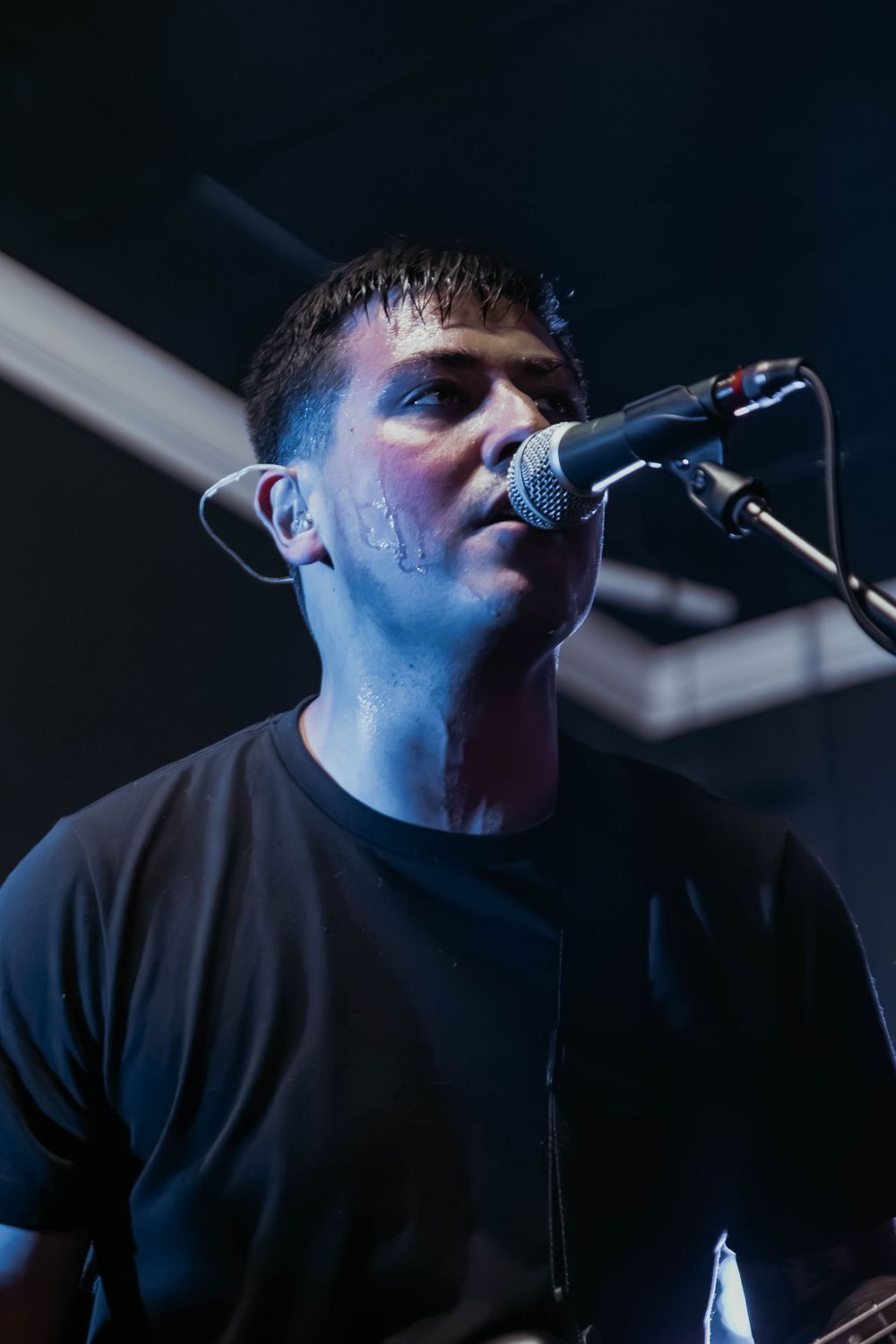 A vocalist performs under dramatic blue lighting while singing into a microphone on stage.