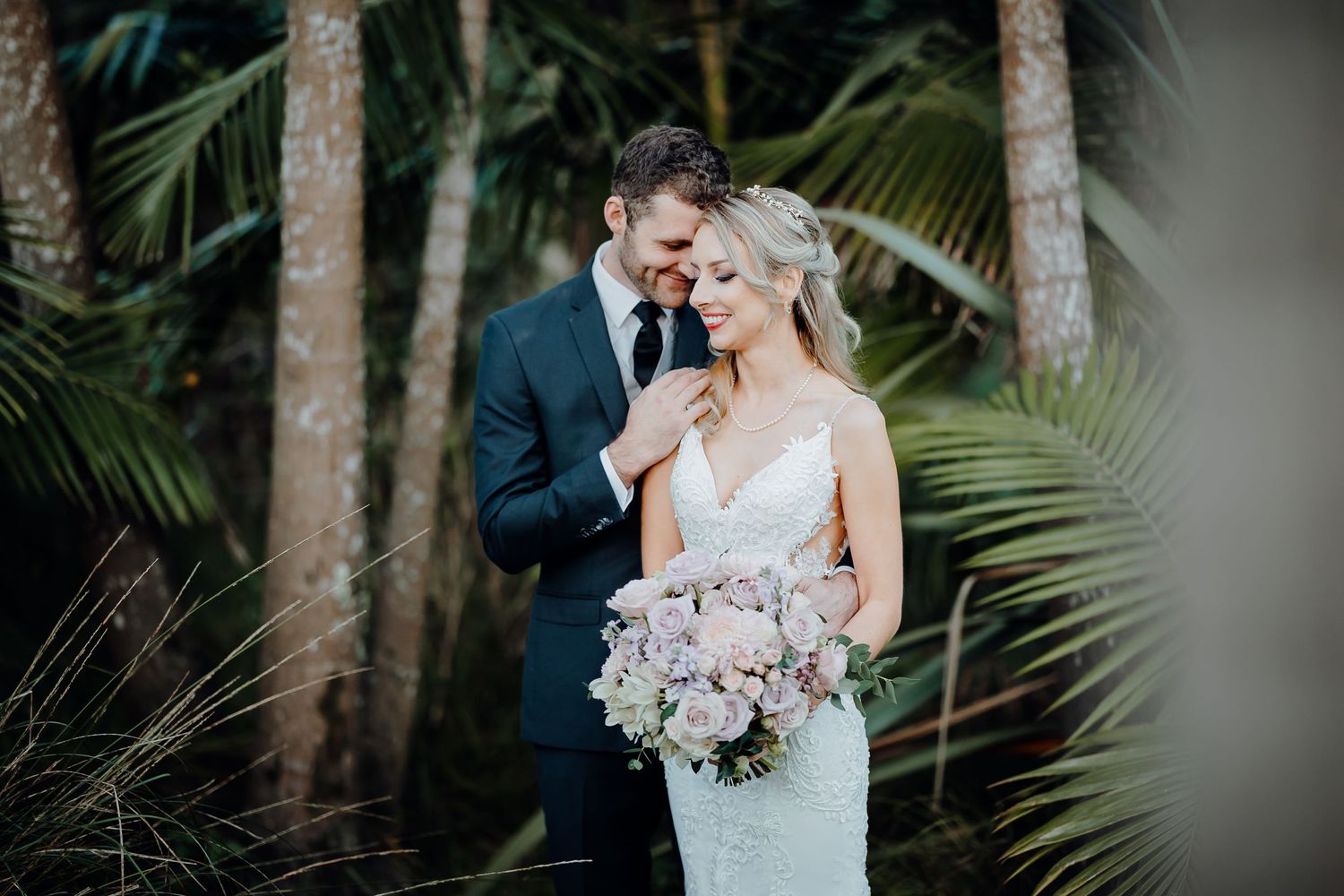 Intimate wedding portrait among tropical palm trees with soft natural lighting.
