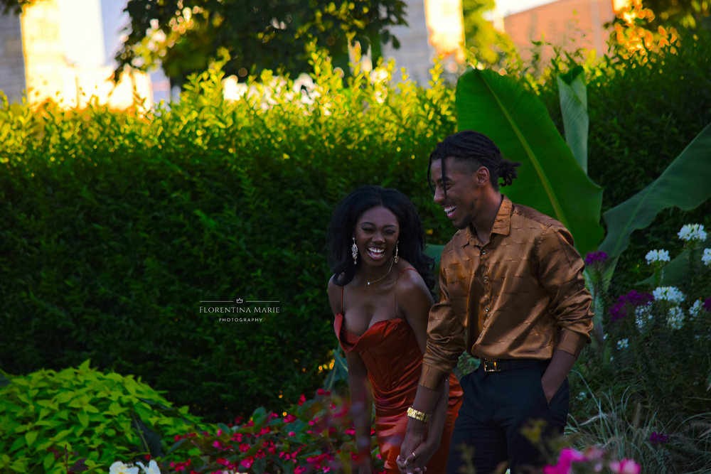 A couple shares a joyful moment in a garden filled with pink flowers and lush greenery.