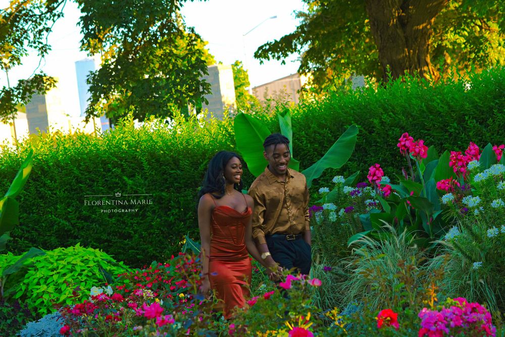 A couple walks through a garden landscape with vibrant flowers and green foliage.