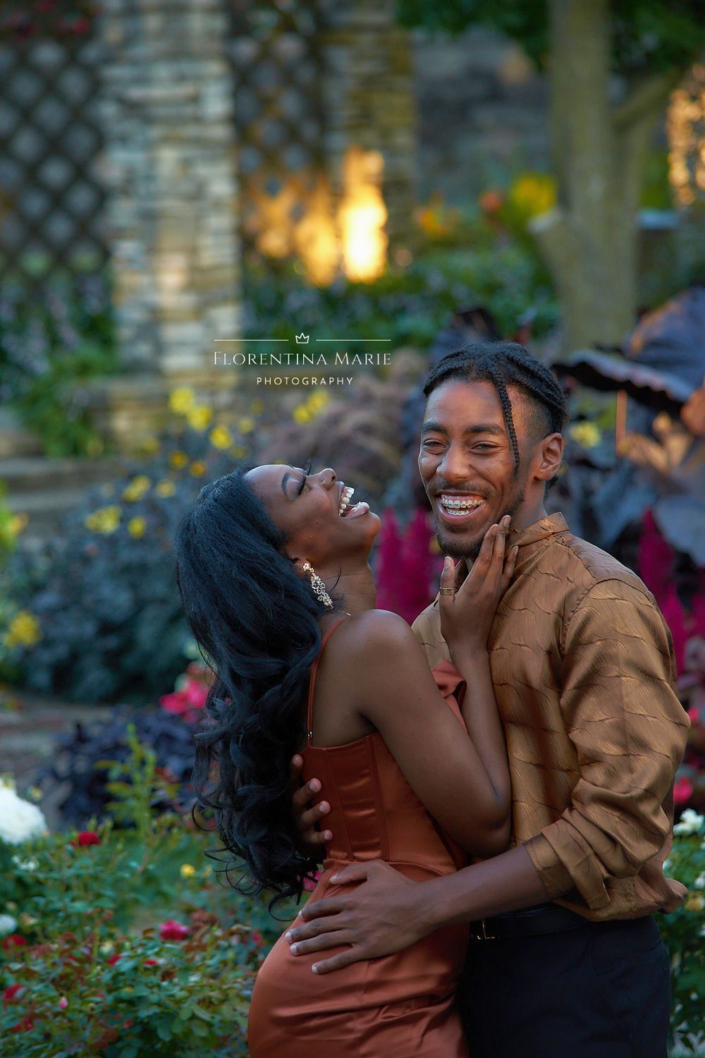 A couple shares a joyful laugh while embracing in a garden with flowers and greenery.