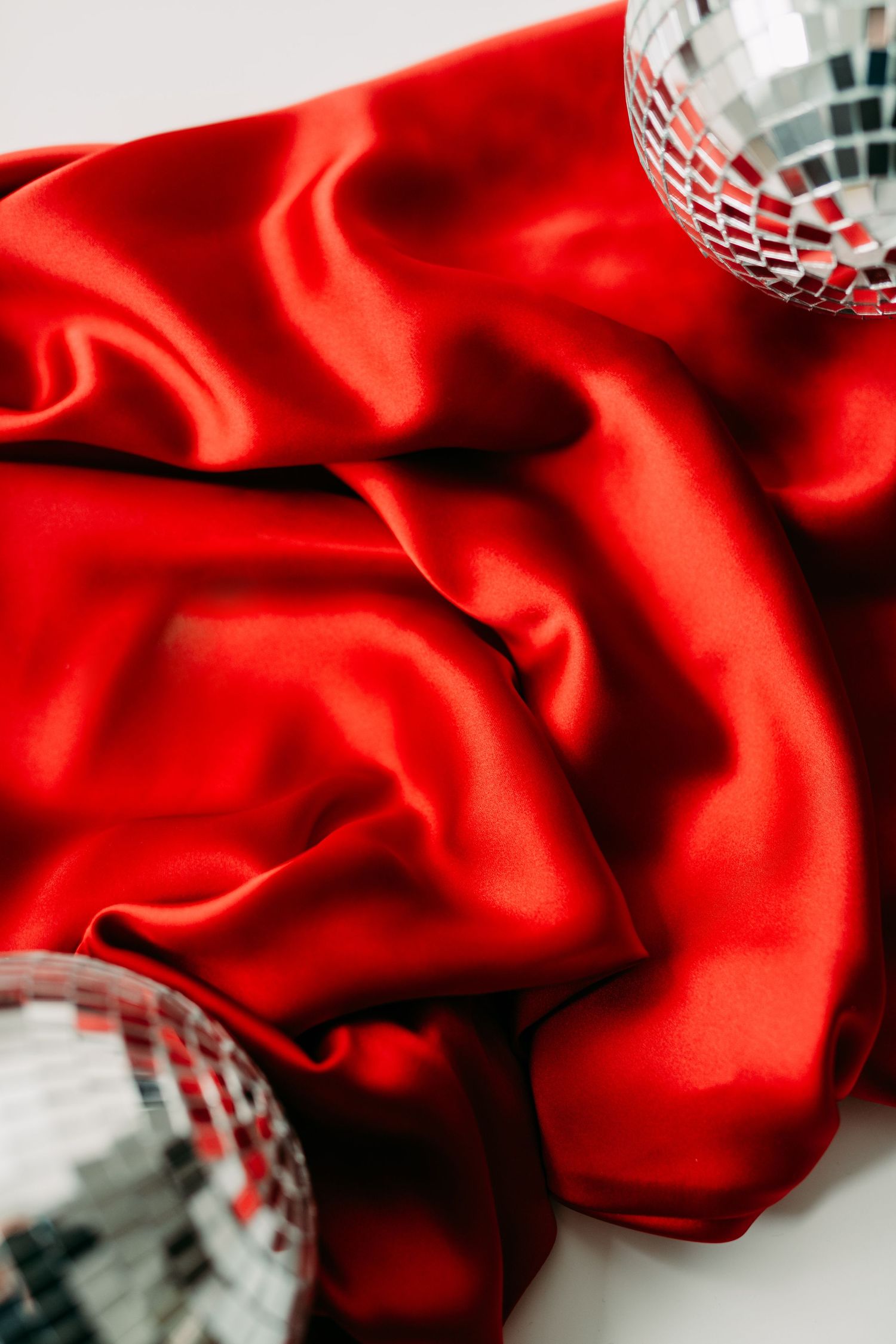 Close-up of disco ball reflecting light on red satin fabric.