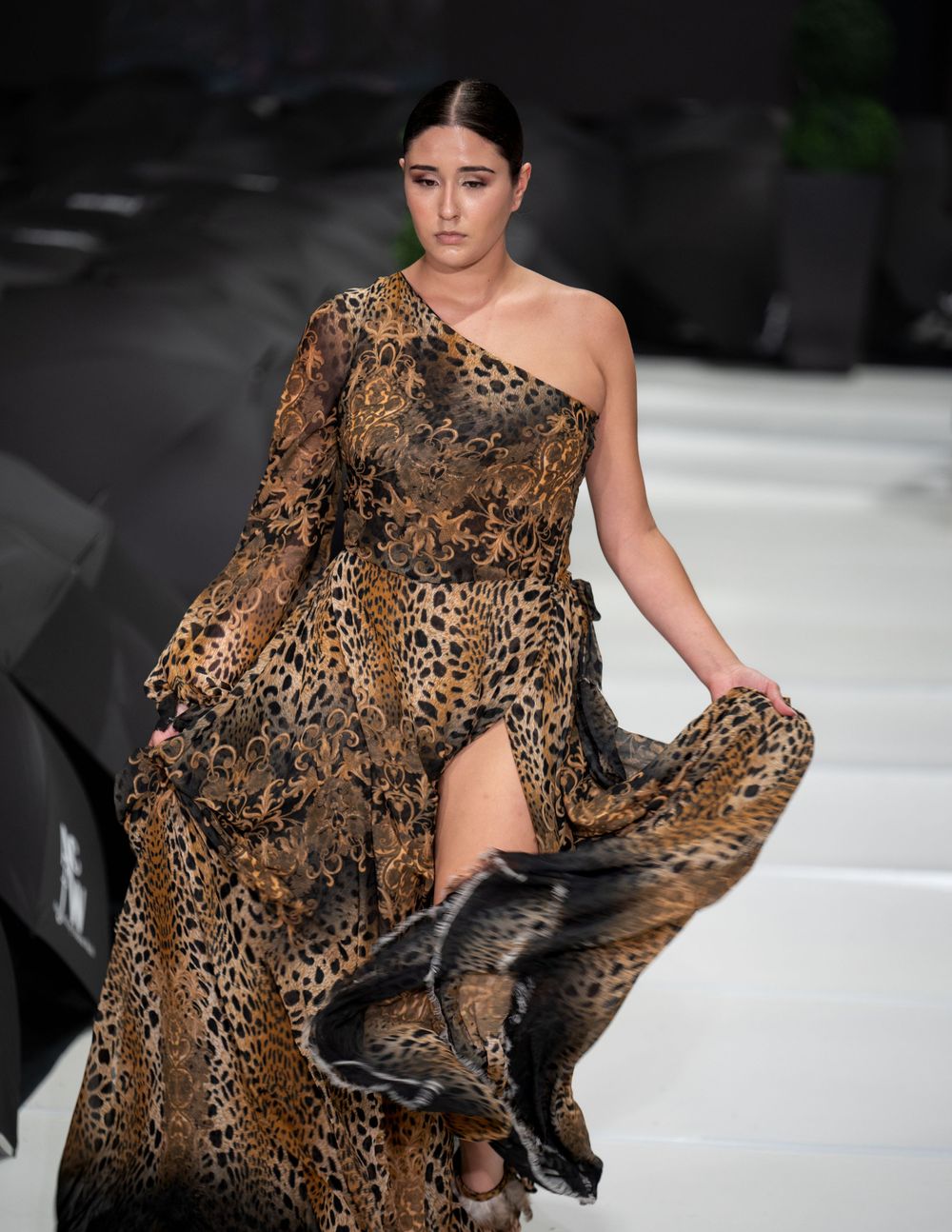 One-shoulder leopard print gown with flowing skirt on fashion runway.