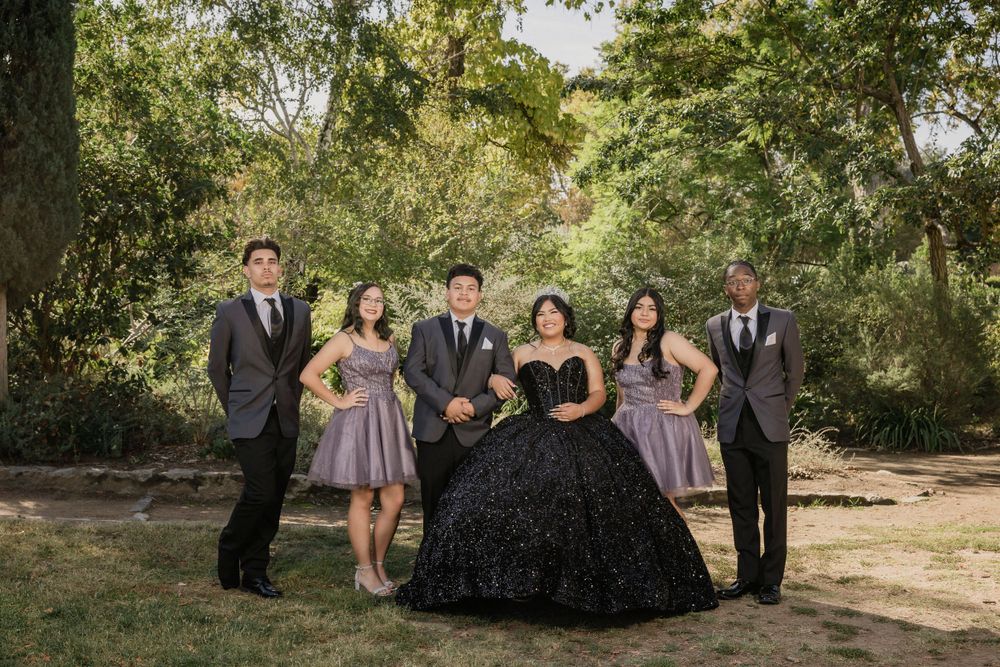 A group photo outdoors with people wearing formal attire including a black ballgown and gray dresses.