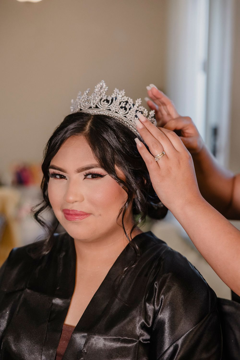 Close-up of preparation moment as ornate crystal tiara is placed on styled dark hair.