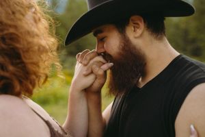 Tender moment between couple in western attire with sunlit mountain backdrop.