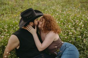 Romantic couple shares intimate moment while sitting in a wildflower field at sunset.