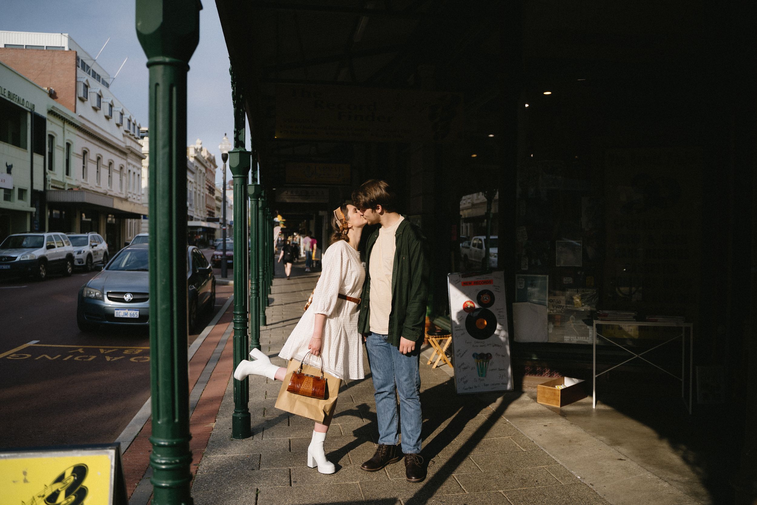 Couple walking down historic city sidewalk with classic architecture and storefronts.