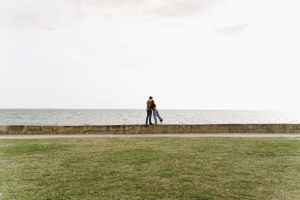 Silhouetted figures standing on stone wall overlooking ocean horizon.