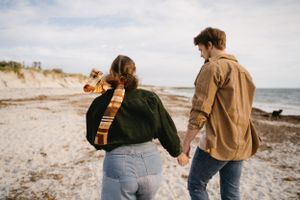 Couple walking hand in hand along a scenic beach shoreline.