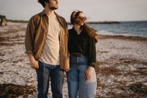 Couple in casual attire enjoying a peaceful moment on a rocky beach.