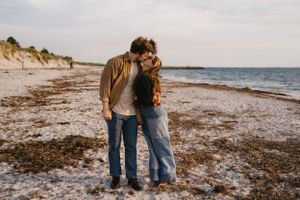 Intimate couple embracing on a serene beach at sunset.