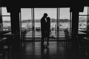 Silhouette of a couple embracing near large windows with a scenic waterfront view.
