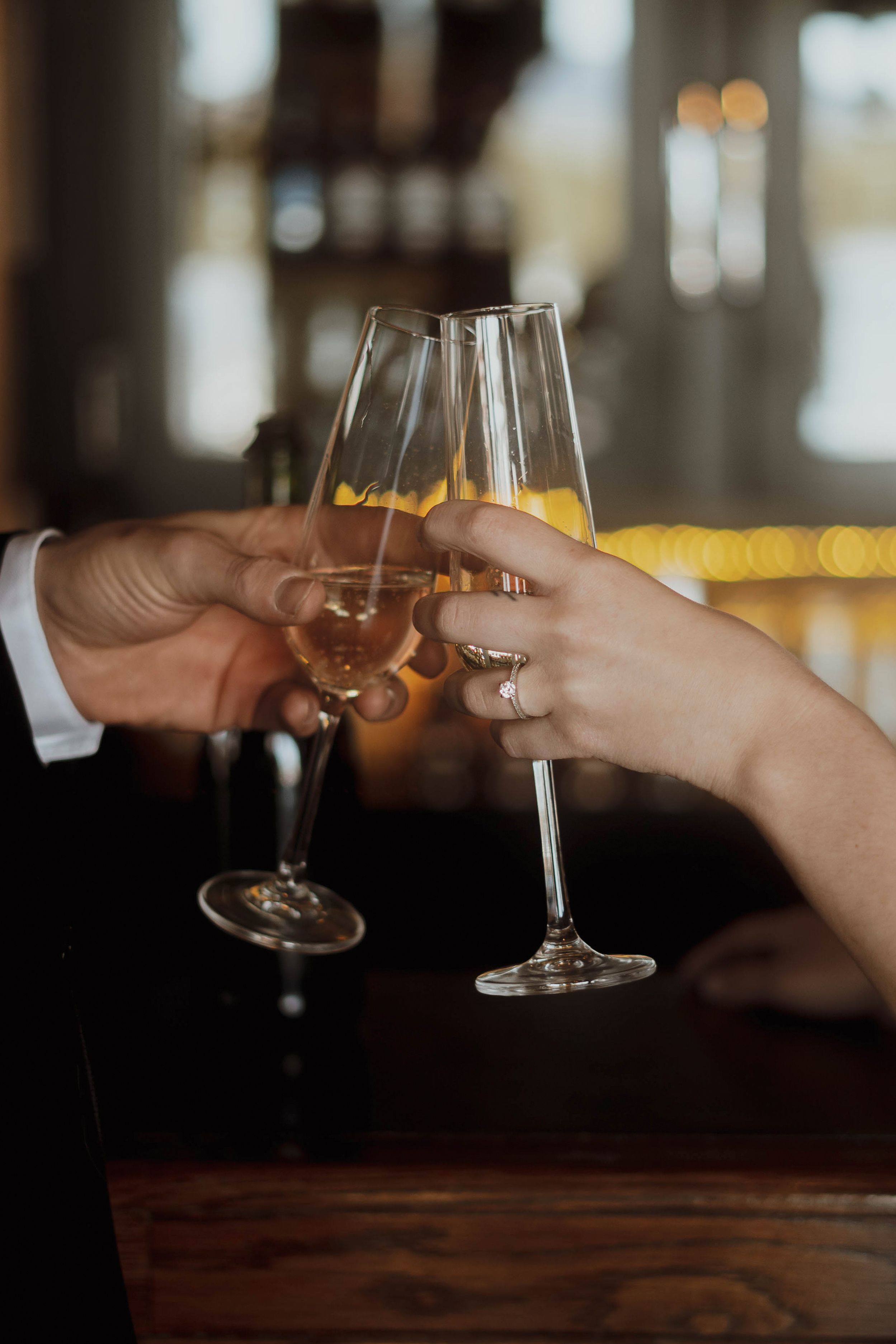Two hands toasting champagne flutes with engagement rings visible.