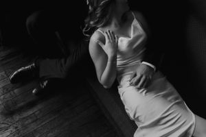 A black and white photo of a person in an elegant white dress lying on a dark floor.