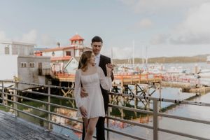 Couple standing on a marina deck with boats and buildings in background.