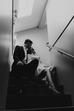 Couple in formal wear sharing a tender moment on dark staircase.