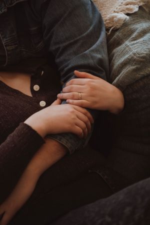 Close-up of intertwined hands with an engagement ring visible against dark fabric.