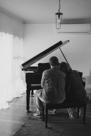 A black and white photo of two people sitting together at a grand piano.