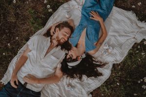 A couple lying on a white blanket outdoors sharing an intimate moment.
