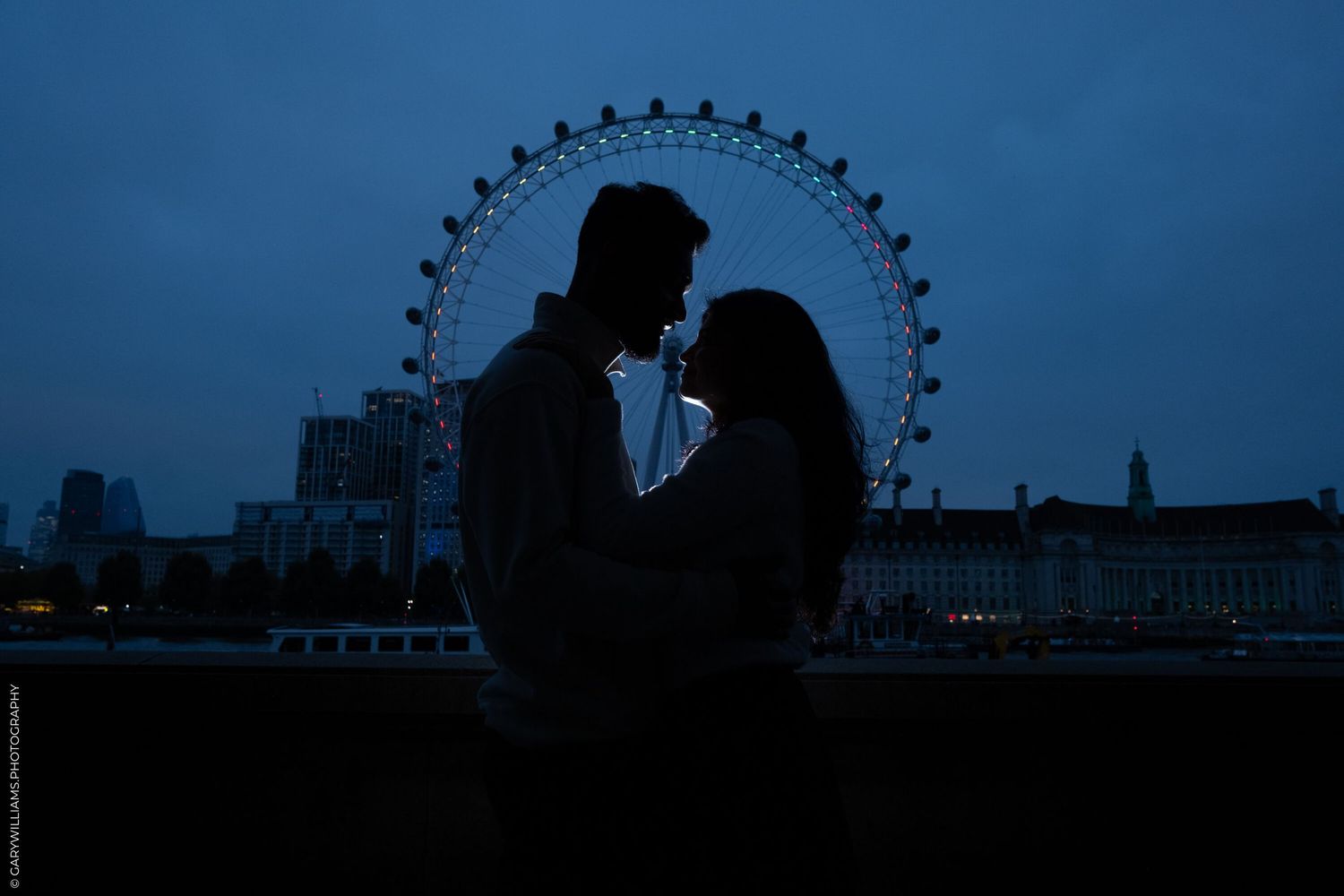 Silhouetted couple against London Eye and twilight sky.