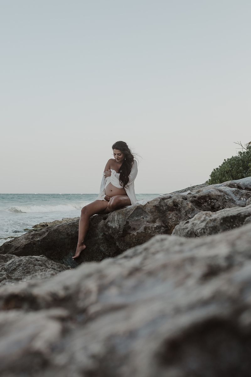 Pregnant woman sitting on Caribbean rocks during maternity session.