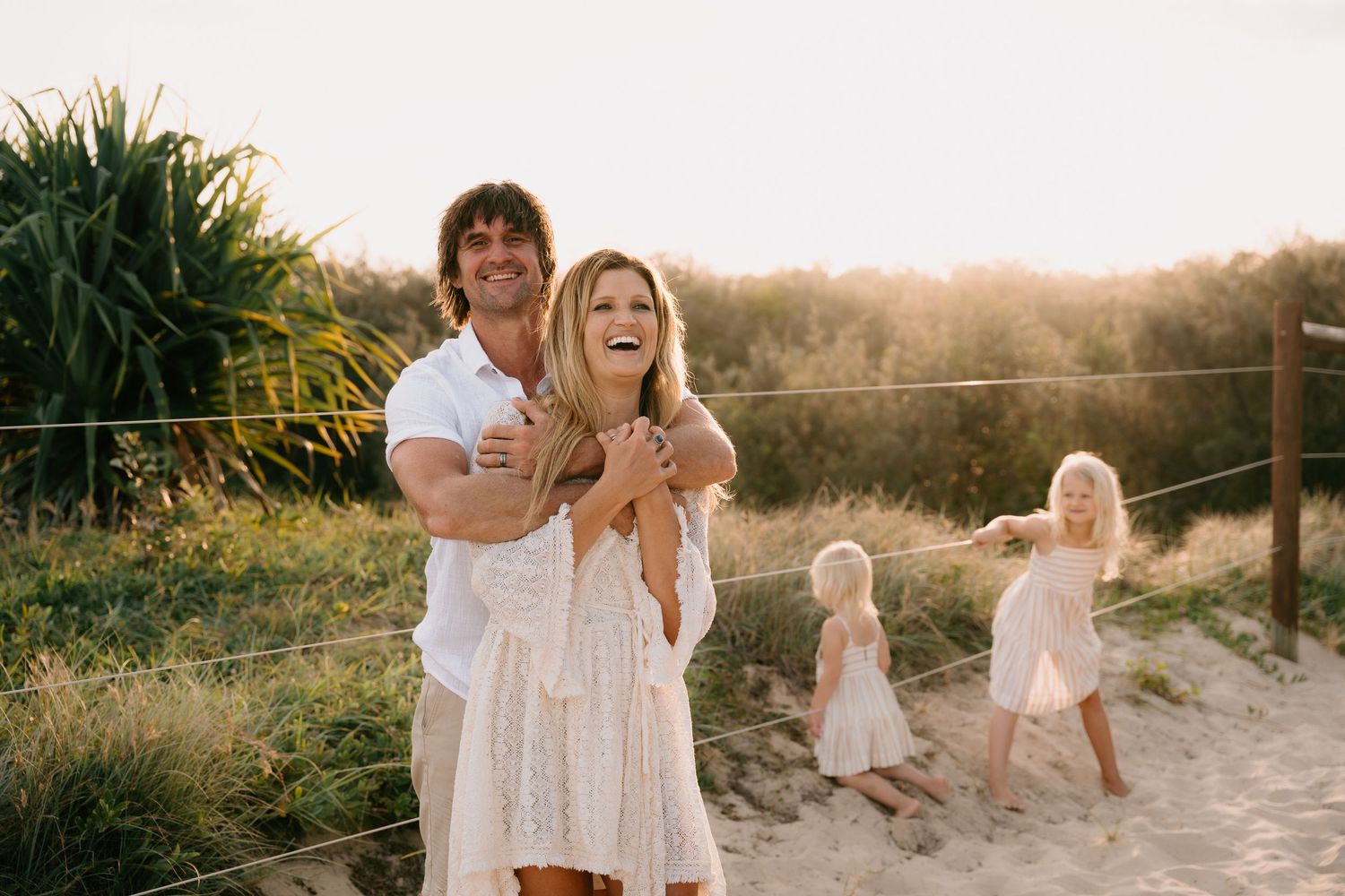 Family playing together on sandy beach path at sunset.