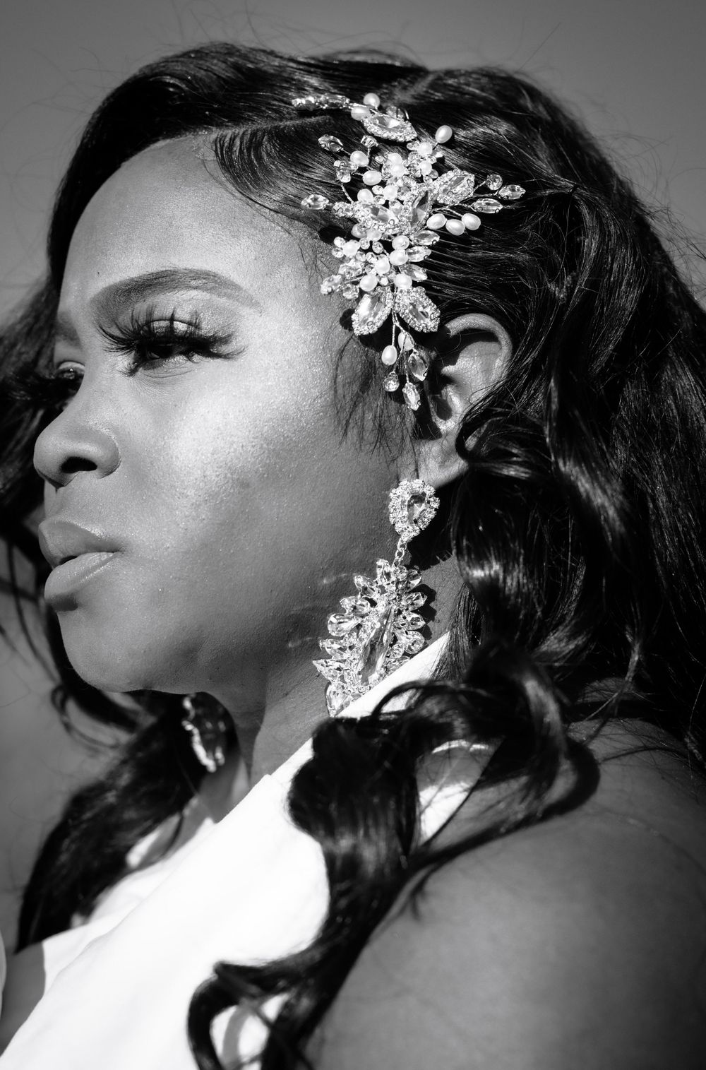 Black and white portrait of a woman wearing crystal hair accessories and chandelier earrings with elegant wavy hair.