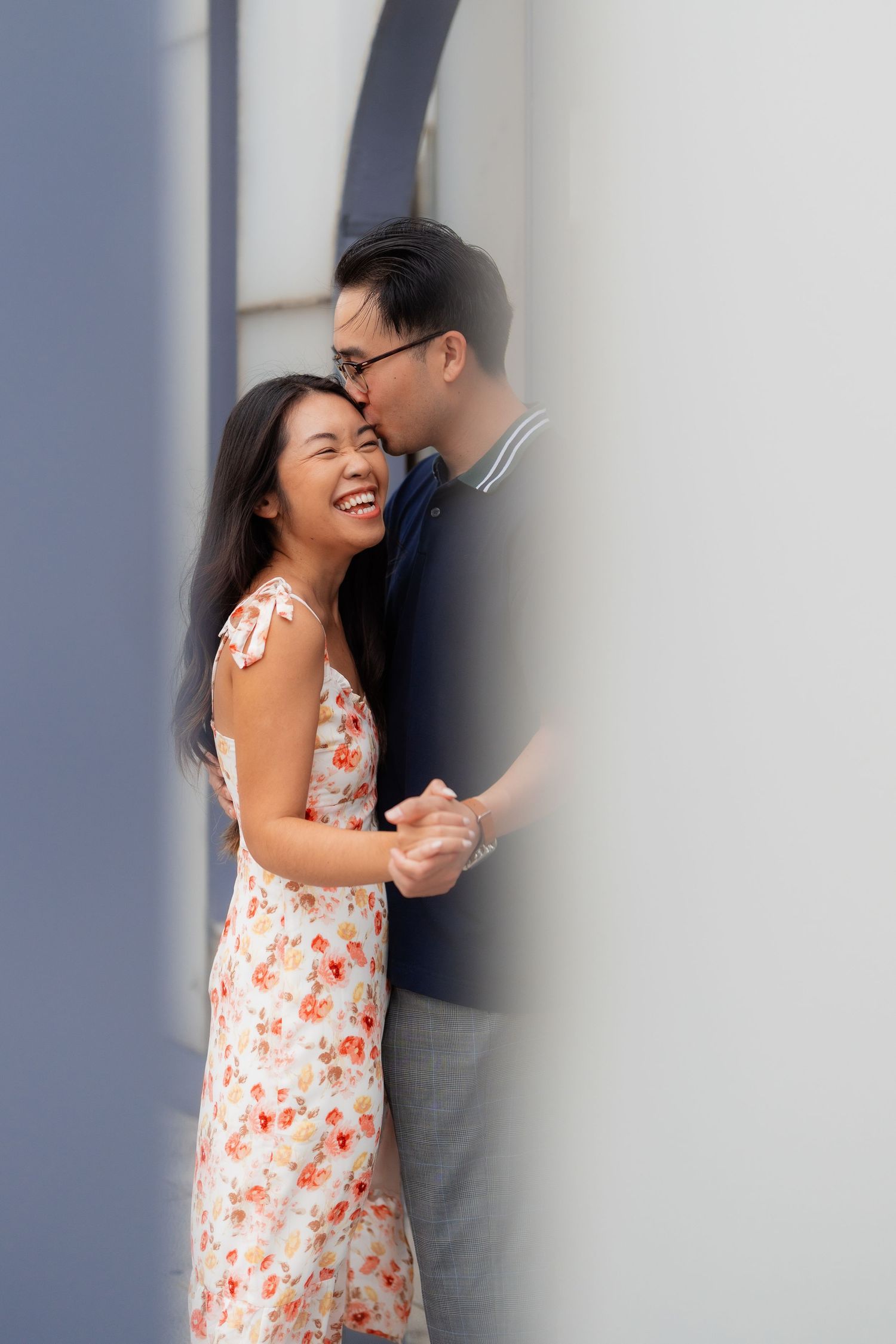 A couple sharing an intimate moment against a white wall with soft lighting.