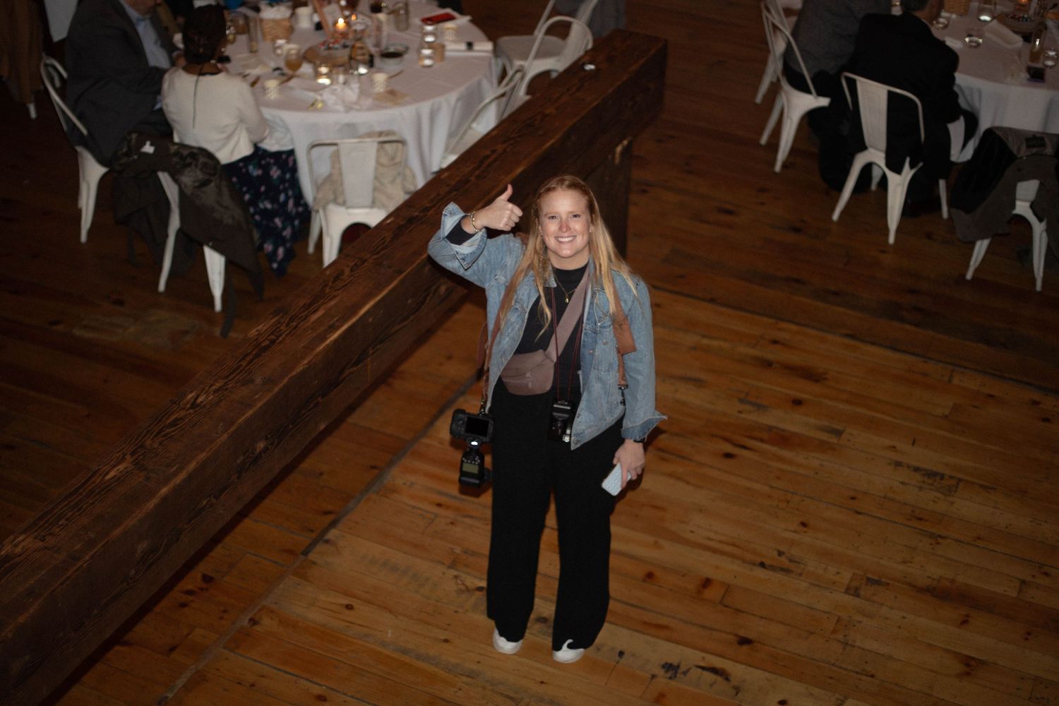 Wedding reception venue with elegant round tables, white linens, and wooden floors in a rustic setting.