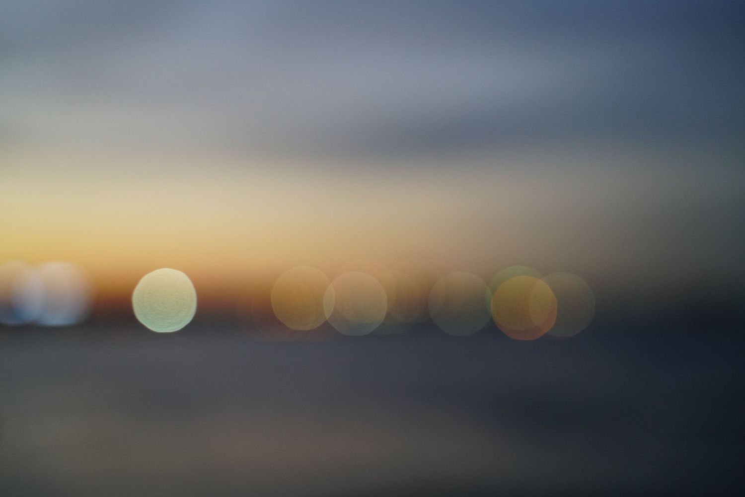 Abstract blurred bokeh lights against a dark background during sunset or sunrise.