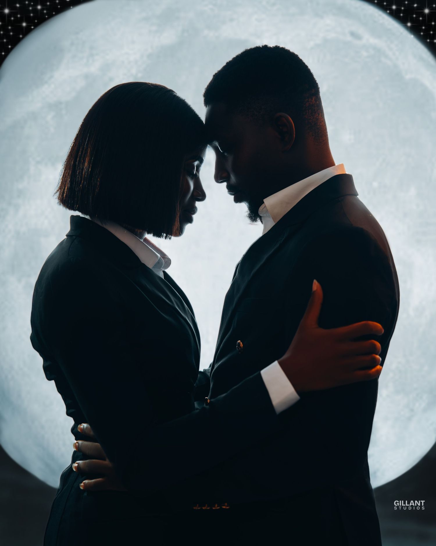 Silhouetted couple in formal wear pose against large moon backdrop.