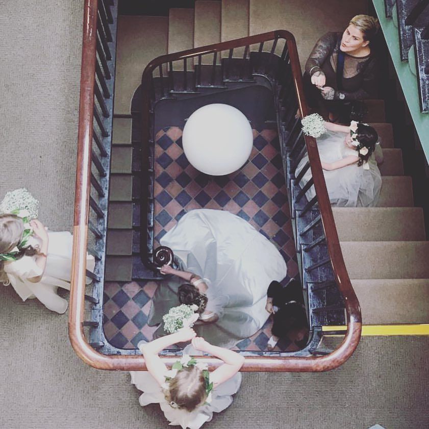 Overhead view of a curved stairwell with vintage patterned carpet and figures dressed in white gowns positioned on steps.