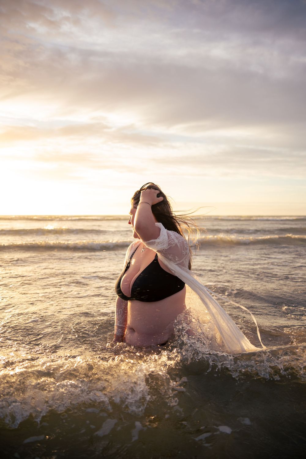 Woman standing in the ocean with a beautiful sunset during a empowerment shoot