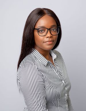 Professional portrait of someone in a black-framed glasses and striped button-up shirt against neutral background.