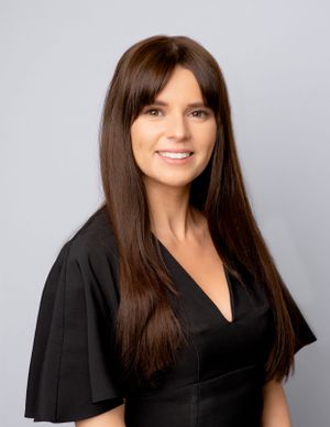 Professional portrait of someone with long dark brown hair wearing a black v-neck top with fluttery short sleeves.